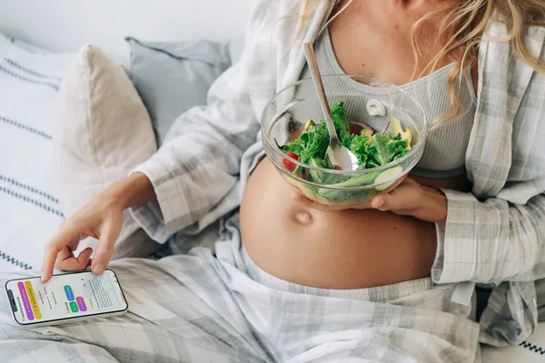 Schwangere isst entspannt einen frischen Salat, daneben liegt ihr Smartphone mit der DiaBelly App